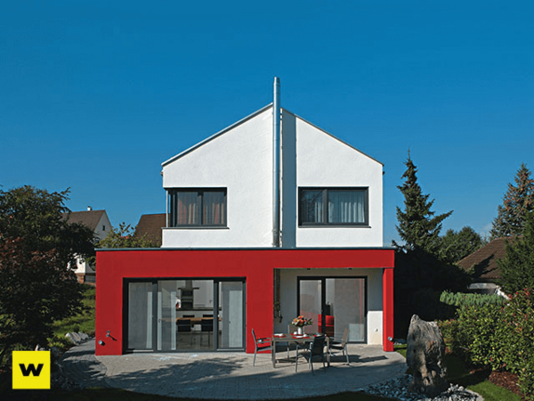 Modernes Einfamilienhaus mit roter Fassade, Flachdach und Garten bei sonnigem Wetter.