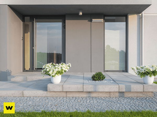 Moderner Hauseingang mit großen Fenstern, grauen Fliesen und weißen Blumenkübeln.