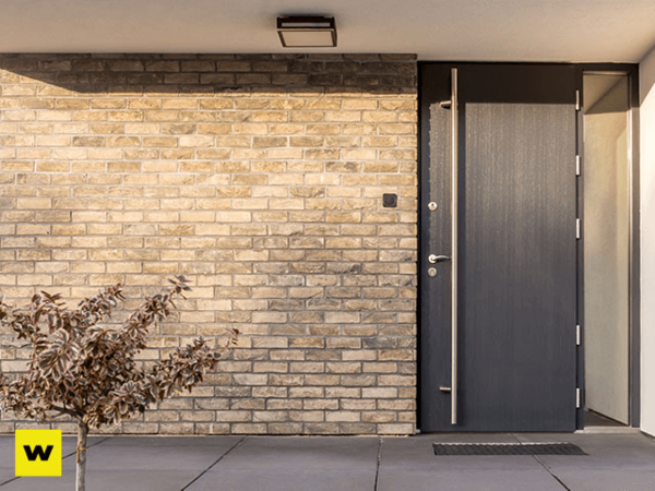 Moderne Haustür aus Aluminium neben heller Klinkerfassade mit eingelassenem Türgriff.