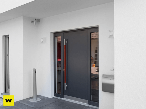 Moderne Haustür aus dunklem Aluminium mit Glaseinsätzen an einem weißen Haus.