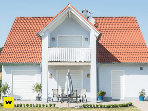 Modernes Einfamilienhaus mit rotem Dach, Terrasse und Rollläden an Fenstern und Türen.